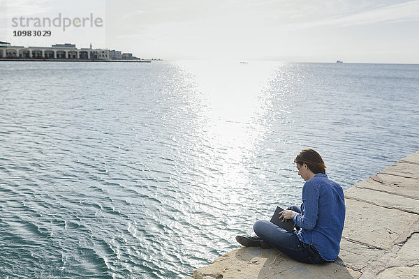 Italien  Triest  junge Frau mit einem Buch auf dem Dock sitzend
