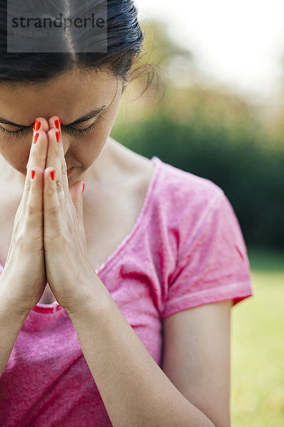 Junge Frau meditiert draußen im Park  Hände  Nahaufnahme  Augen geschlossen