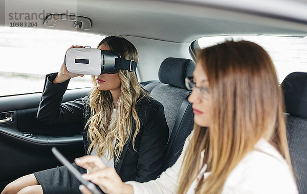 Zwei Geschäftsfrauen mit VR-Brille und digitalem Tablett im Auto