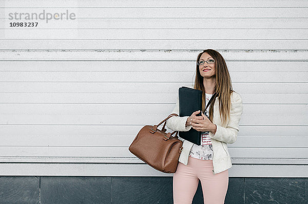 Lächelnde Geschäftsfrau mit Handtasche und Mappe im Freien