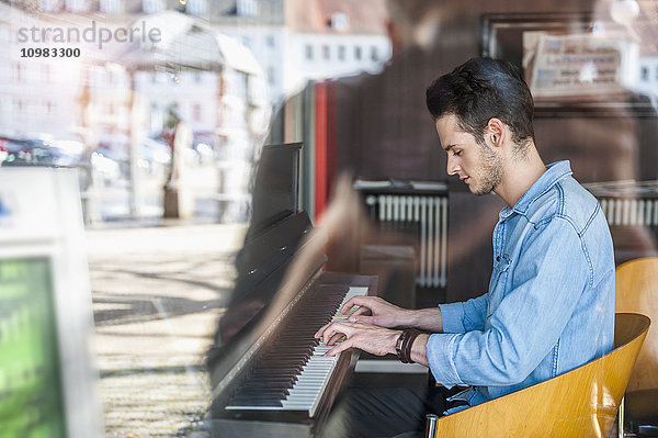 Junger Mann spielt Klavier in einem Cafe