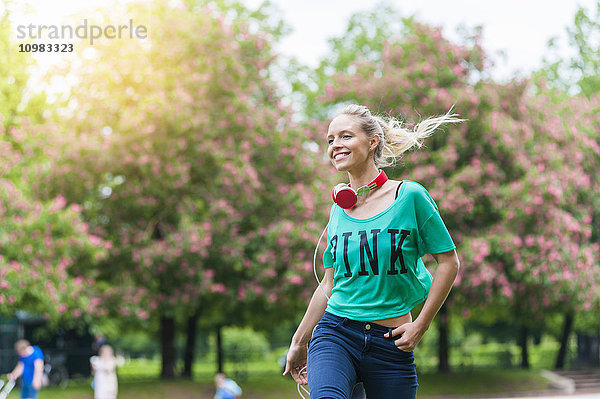 Fröhliche blonde Frau mit Kopfhörer im Park
