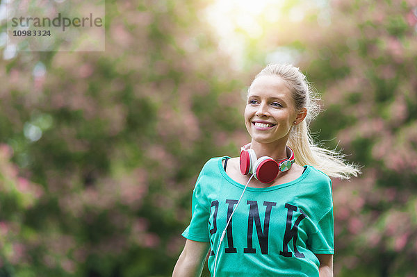 Porträt einer glücklichen blonden Frau mit Kopfhörer im Park