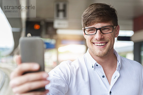 Lächelnder junger Mann am Bahnsteig mit einem Selfie