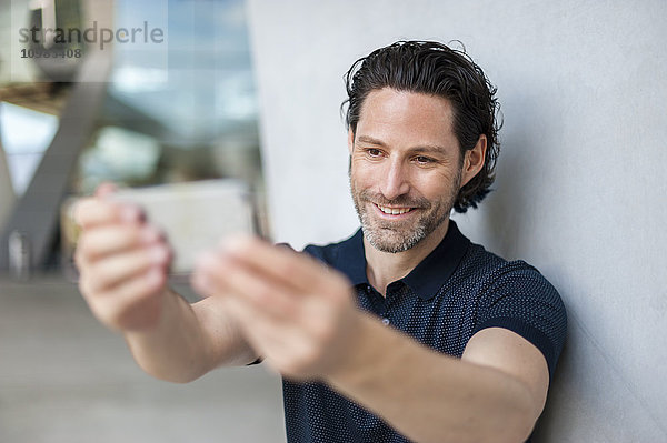 Porträt eines lächelnden Mannes  der sich selbst mit dem Handy fotografiert.