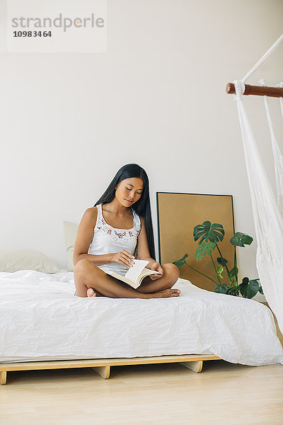 Junge Frau auf dem Bett sitzend Lesebuch