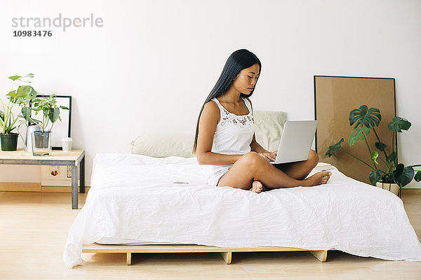 Junge Frau auf dem Bett sitzend mit Laptop