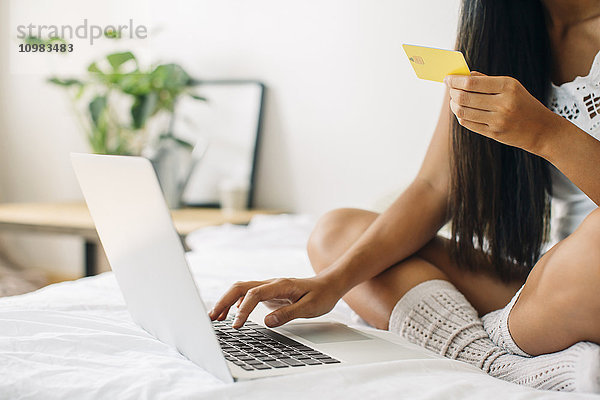 Junge Frau auf dem Bett sitzend online einkaufen