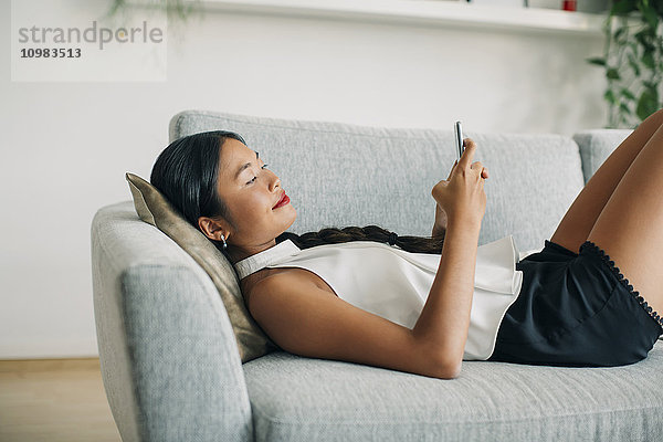 Junge Frau auf der Couch liegend mit dem Handy
