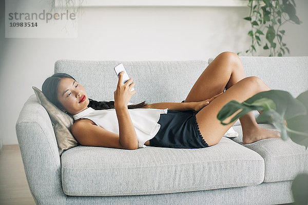 Junge Frau auf der Couch liegend mit dem Handy