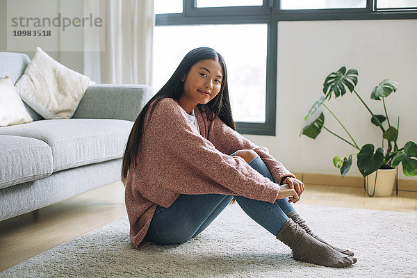 Porträt einer lächelnden jungen Frau  die zu Hause auf dem Boden sitzt.