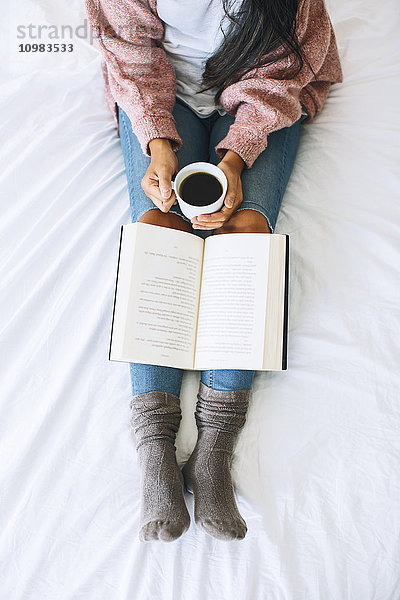 Frau mit Tasse Kaffee und Buch Entspannung auf dem Bett  Teilansicht