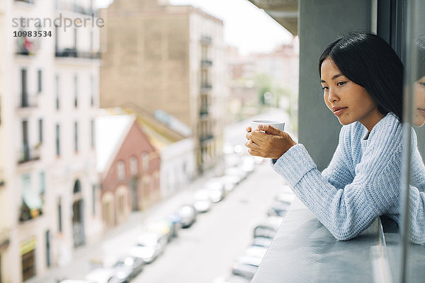 Junge Frau mit Tasse Kaffee aus dem Fenster gelehnt