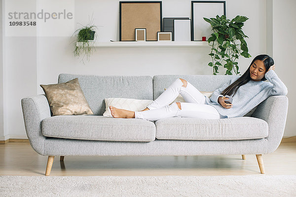 Junge Frau entspannt auf der Couch im Wohnzimmer mit Smartphone