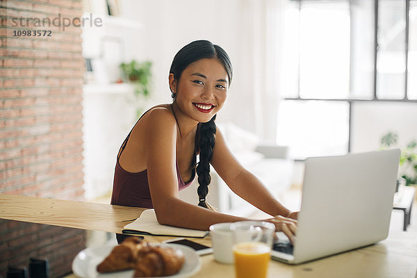 Porträt einer lächelnden Frau bei der Arbeit mit dem Laptop zu Hause