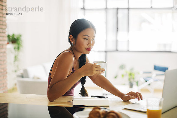 Frau mit Tasse Kaffee bei der Arbeit mit dem Laptop zu Hause