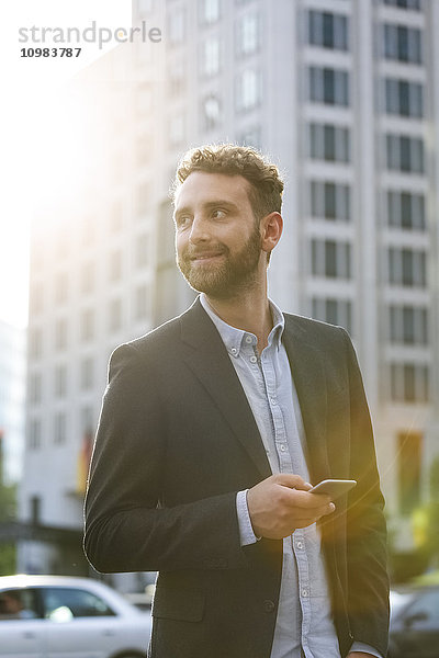 Lächelnder junger Geschäftsmann mit Handy im Freien