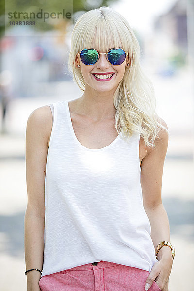 Porträt einer lächelnden blonden Frau mit verspiegelter Sonnenbrille