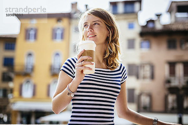 Italien  Udine  Portrait einer lächelnden jungen Frau mit Kaffee zum Mitnehmen