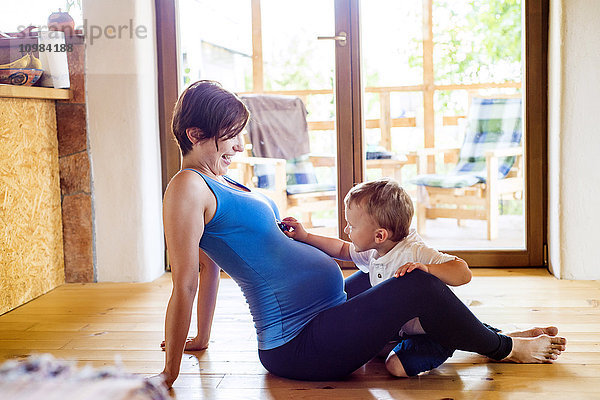 Schwangere Mutter spielt mit ihrem kleinen Sohn auf dem Boden.