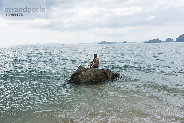 Thailand  Tubkaek  Rückansicht einer Frau  die auf einem Felsen sitzt und auf das Meer schaut.