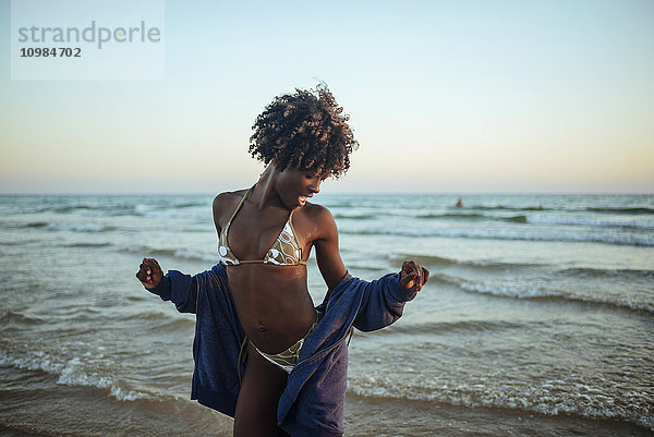 Fröhliche junge Frau  die bei Sonnenuntergang am Meer tanzt.