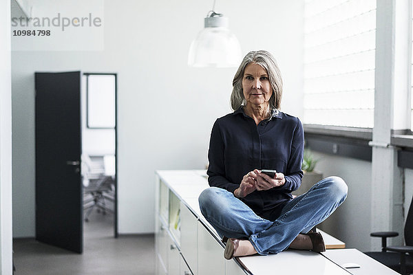 Seniorin auf einem Schrank im Büro sitzend