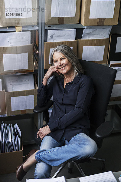 Lächelnde Seniorin sitzt auf Bürostuhl in einer Fabrik