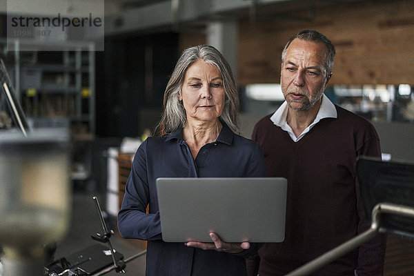 Senior Frau und Mann in einer Druckerei mit Blick auf Laptop