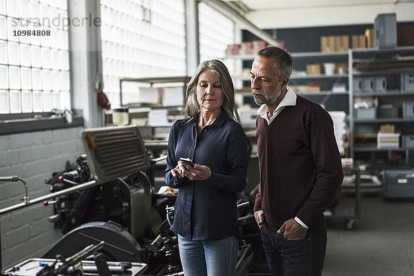 Senior Frau und Mann in einer Druckerei mit Blick auf Handy