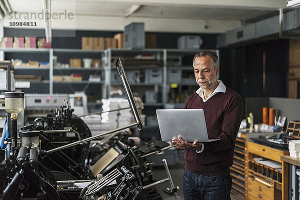 Mann in einer Druckerei mit Blick auf Laptop