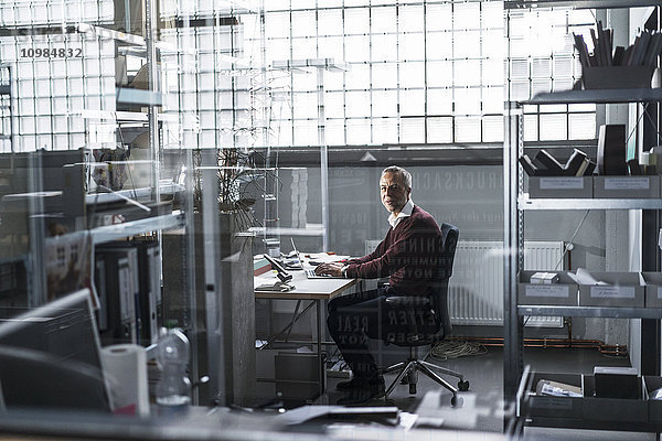 Erwachsener Mann mit Laptop am Schreibtisch in einer Fabrik