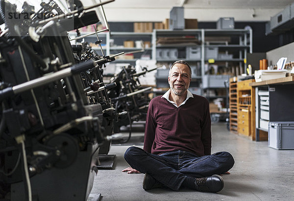 Lächelnder reifer Mann sitzt auf dem Boden einer Druckerei
