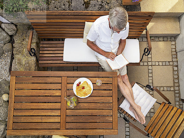 Älterer Mann auf der Terrasse sitzend Lesebuch