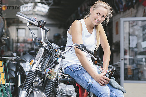 Lächelnde junge Frau mit Bierflasche auf dem Motorrad