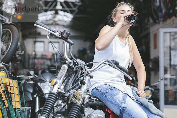 Junge Frau trinkt Bier aus der Flasche auf dem Motorrad