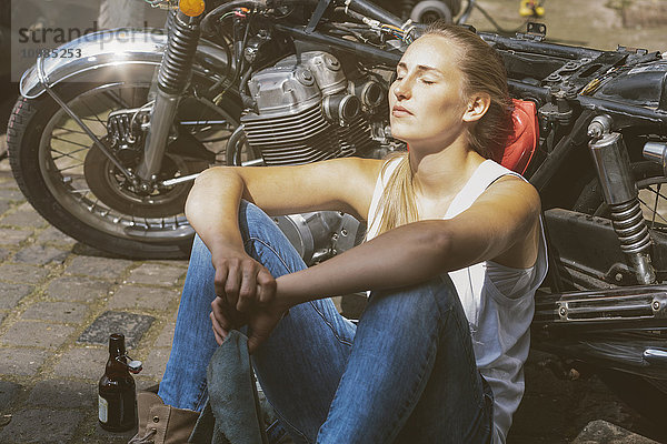 Junge Frau mit Bierflasche am Motorrad lehnend
