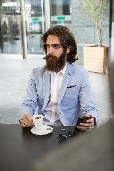Stilvoller Geschäftsmann mit Handy im Café