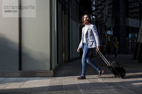 Stilvoller Geschäftsmann beim Spaziergang mit Koffer im Freien