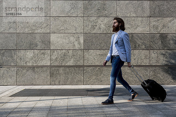 Stilvoller Geschäftsmann beim Spaziergang mit Koffer im Freien