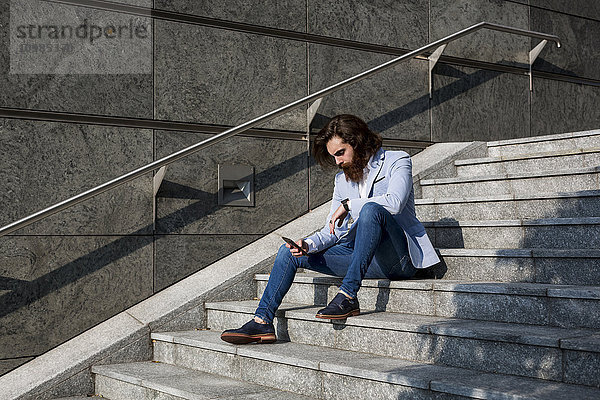 Stilvoller Geschäftsmann mit Handy auf der Treppe im Freien