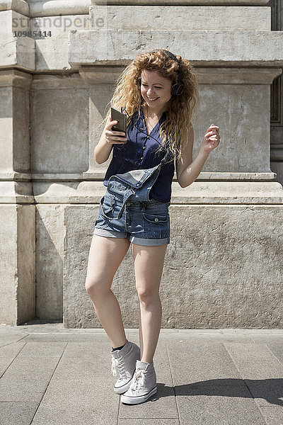 Lächelnde junge Frau mit Kopfhörer und Smartphone