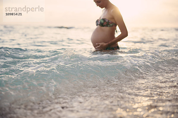 Schwangere Frau im Meer stehend bei Gegenlicht