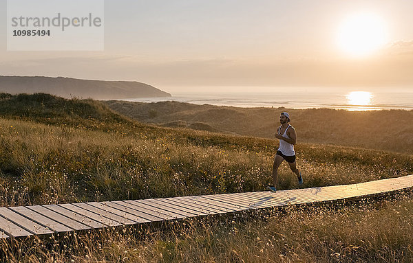 Spanien  Aviles  Sportler  der bei Sonnenuntergang einen Küstenweg entlang läuft.