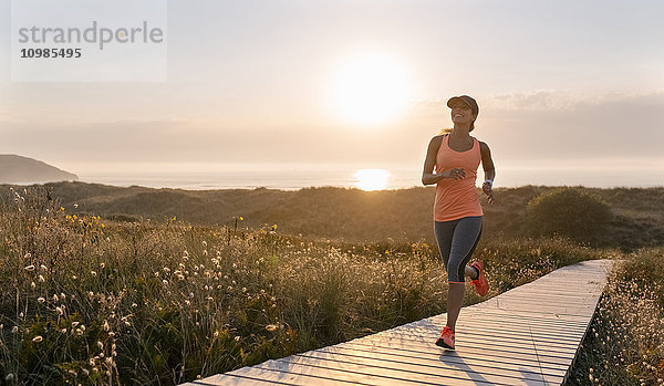 Spanien  Aviles  junge Sportlerin  die bei Sonnenuntergang einen Küstenweg entlang läuft