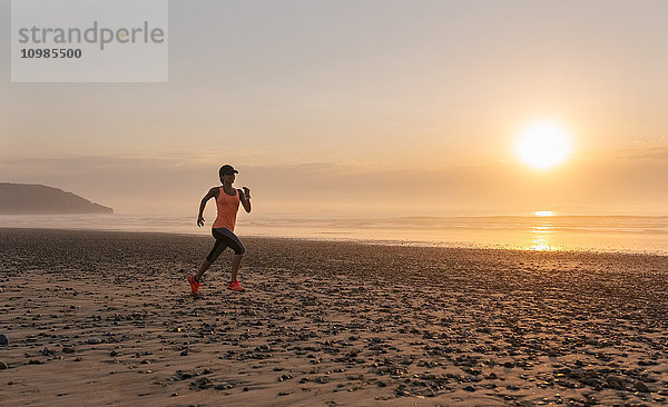 Sportlerin beim Laufen am Strand bei Sonnenuntergang