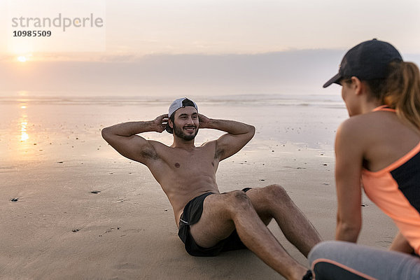 Sportlerpaar beim Training am Strand bei Sonnenuntergang