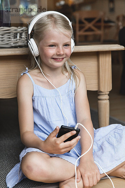 Porträt eines glücklichen kleinen Mädchens beim Musikhören mit Kopfhörer und Smartphone