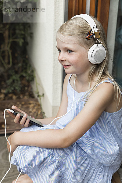 Lächelndes kleines Mädchen beim Musikhören mit Kopfhörer und Smartphone