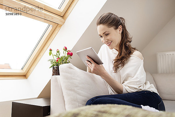 Lächelnde Frau auf der Couch sitzend mit digitalem Tablett